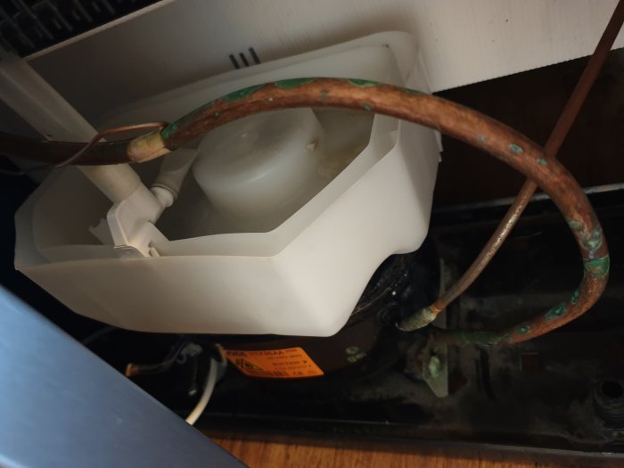 Bild på en kylskåpskompressor med torkat gegga och rostiga rör.
