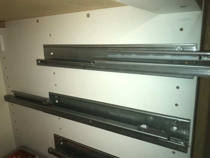 Metallådskenssystem monterade på insidan av ett vitt skåp, eventuellt inte matchande IKEA Rationell.
