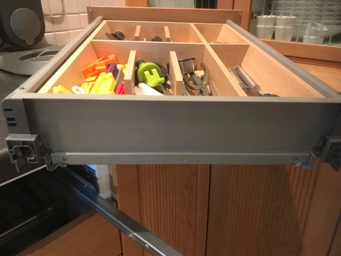 Öppen kökslåda med skenorna synliga och bestickorganisatör innehållande köksredskap.