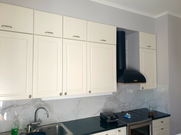 Nykaklat kök med vita skåp, granitklinkers och en mörk köksfläkt mot en marmorerad vägg.