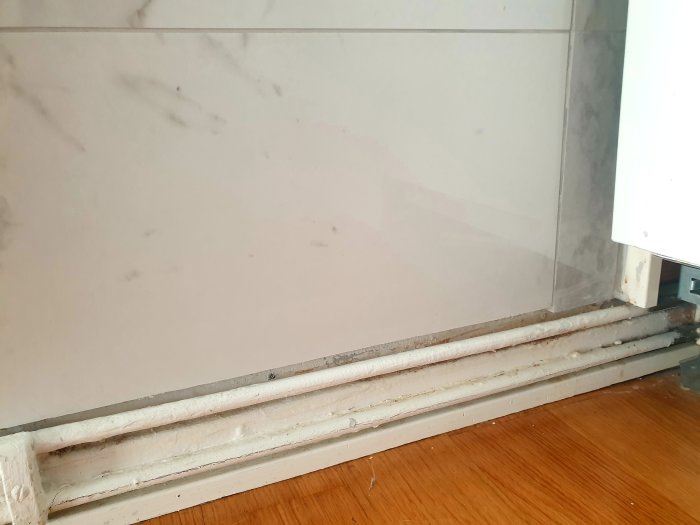 Granitklinkers på vägg nära golv med elementrör, synliga skarvar och ojämna kanter mot väggen.