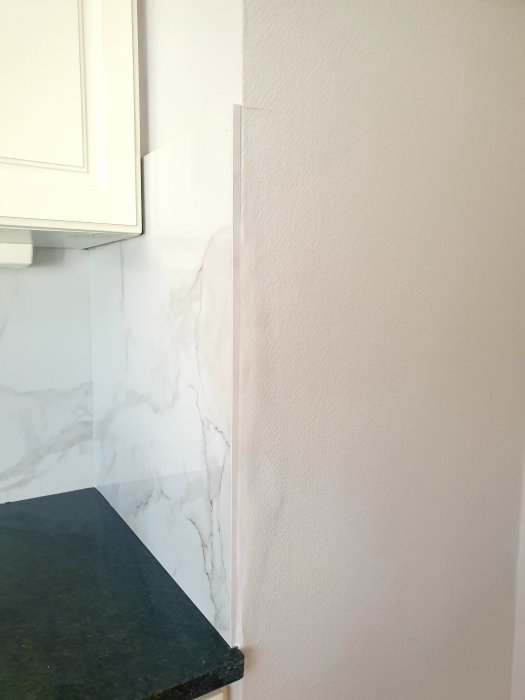 Kök med marmormönstrade kakelplattor och en synlig skarv vid köksskåpet i en ände.