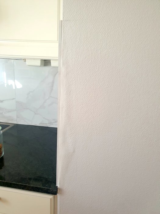 Kök med granitklinkers och väggkant där kakel möter tapet nära hörn och köksskåp.