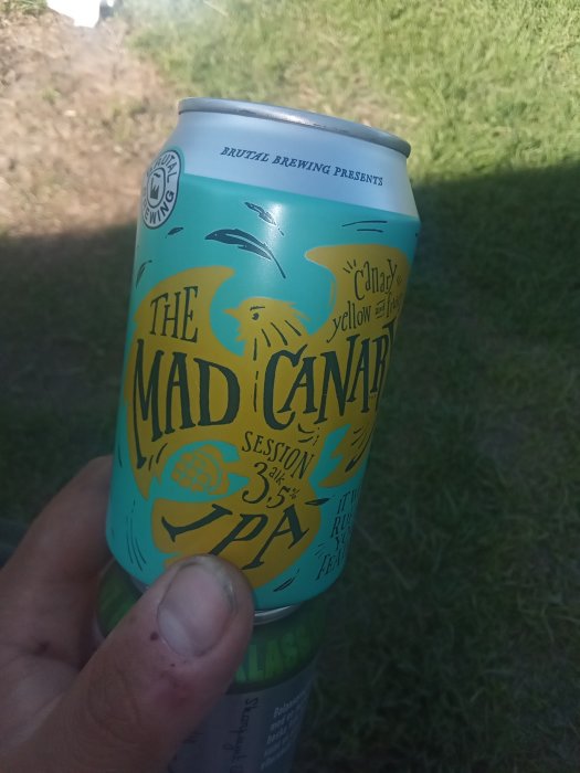 Hand håller en färgglad burk öl märkt "The Mad Canary Session IPA" ute i grön miljö.