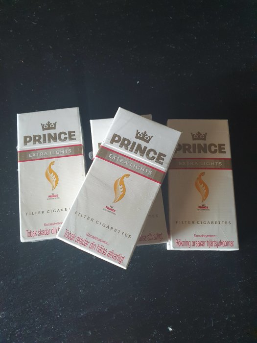 Tre paket Prince Extra Lights-cigaretter utan varningstexter på bord.