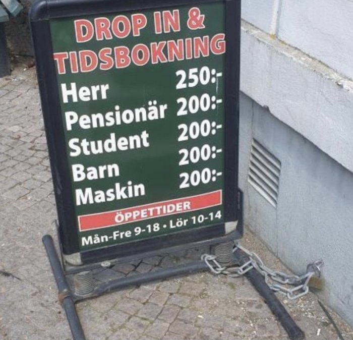 Skylt med priser för olika kundkategorier för drop in och tidsbokning, kedjad vid en stolpe.