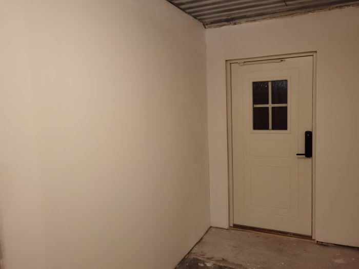 Renoverad hall med vitmålade väggar och en vit dörr med fönster och digitalt lås.