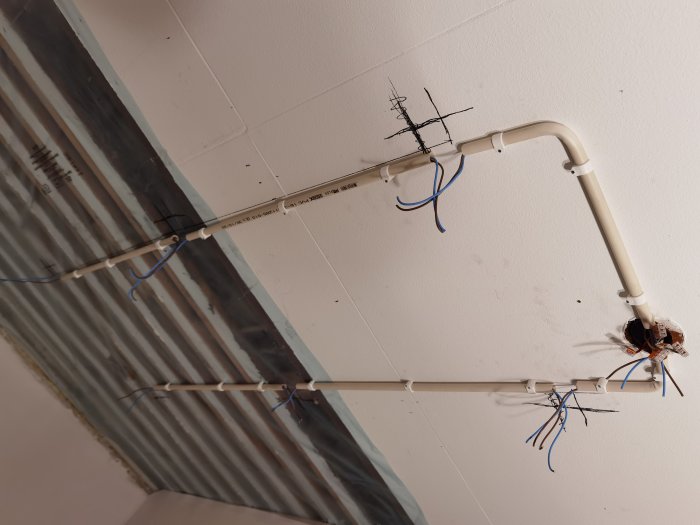 Elektriska installationer med rör och utstickande kablar i ett tak under renovering.