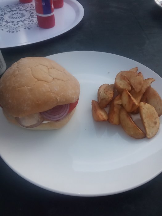 Hamburgare med lök på tallrik bredvid kryddade potatisklyftor.