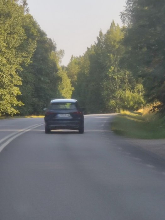 Bil kör på en kurvig landsväg med skog på båda sidor, inga synliga cyklister.