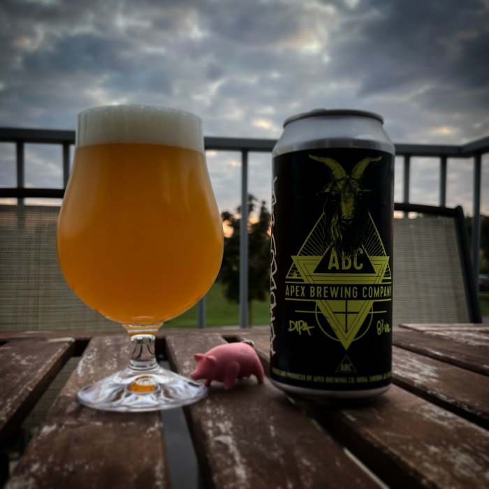 Ölglas fullt med öl bredvid en ölburk på ett träbord mot en bakgrund av en skymningshimmel.