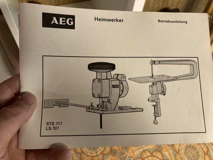 Framsida av en AEG Heimwerker bruksanvisning med illustration av slip- och sågverktyg, borrmaskin saknas.