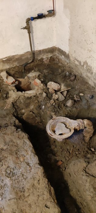 Uppgrävd källargolv med gammal avloppsbrunn och synliga rör vid en husrenovering.