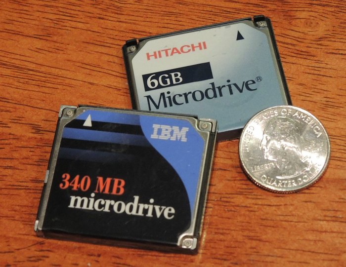 Två IBM Microdrive hårddiskar på 340 MB och 6 GB jämte en amerikansk kvartsdollar på ett träbord.