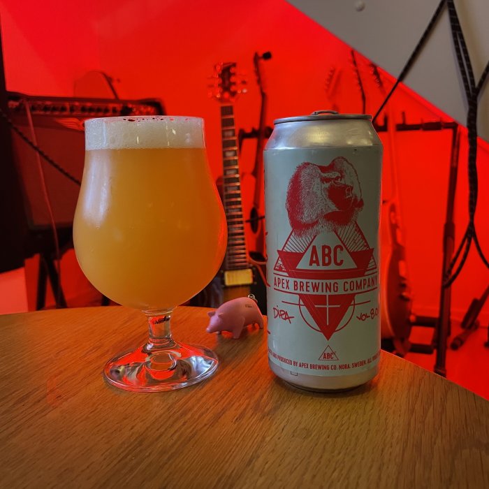 Ett glas öl bredvid en ölburk från Apex Brewing Company på ett bord med musikinstrument i bakgrunden.