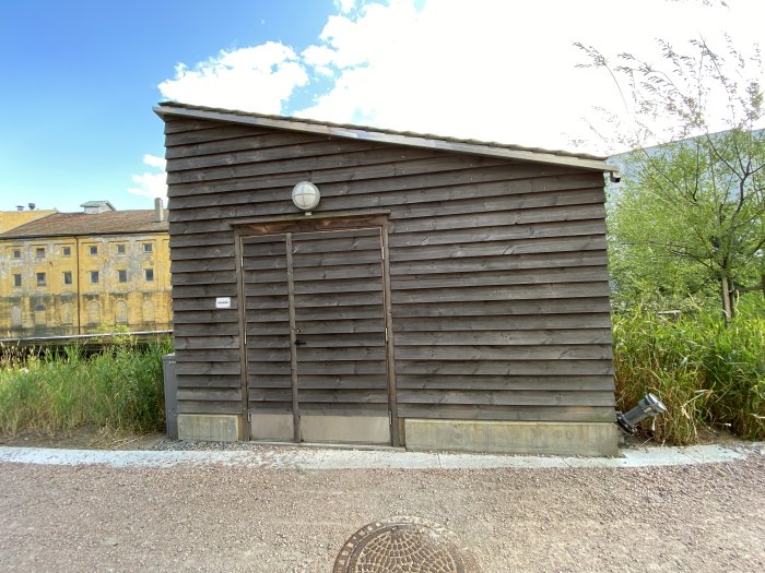 En träbyggnad med diagonalt liggande plattak och träpaneler på fasaden.