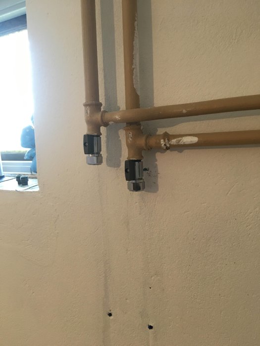 Nymonterade ventilerna på kopparledningar mot en vit vägg.