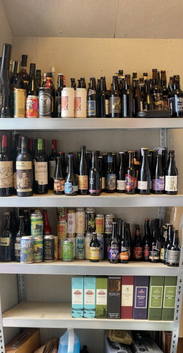 Hyllor i ett förråd fyllda med en omfattande samling av ölflaskor, burkar och vinflaskor i olika storlekar och märken.