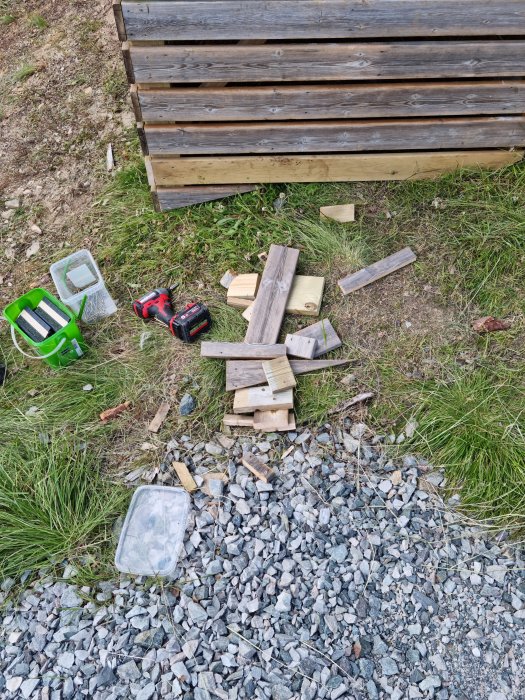 Resterna av en gammal trätrall med spillbitar, ett verktyg och byggmaterial på marken.