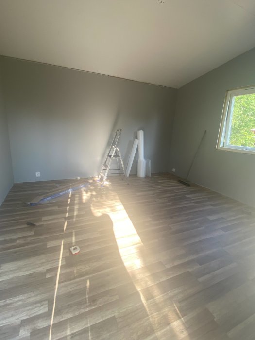 Nytt golv i en gäststuga med solstrålar som faller in genom fönstret och verktyg på golvet.