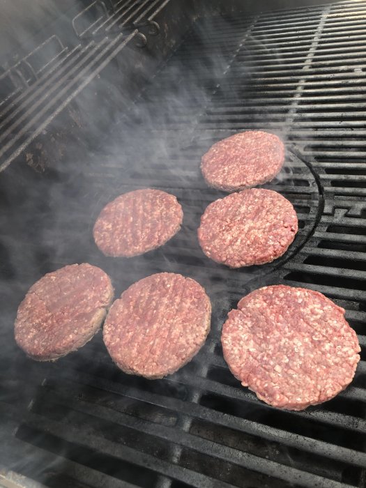 Hamburgare som grillas på en utomhusgrill med rök som stiger upp