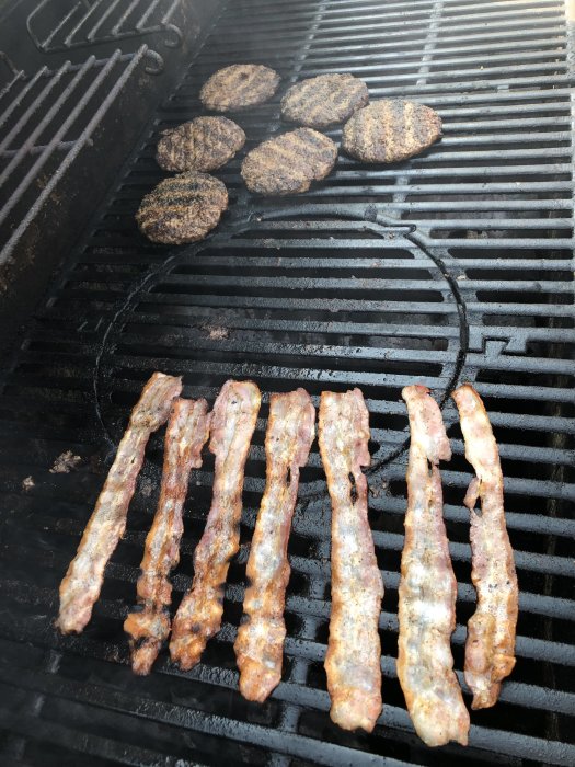 Hamburgare och baconstrimlor som grillas på en grillrist.