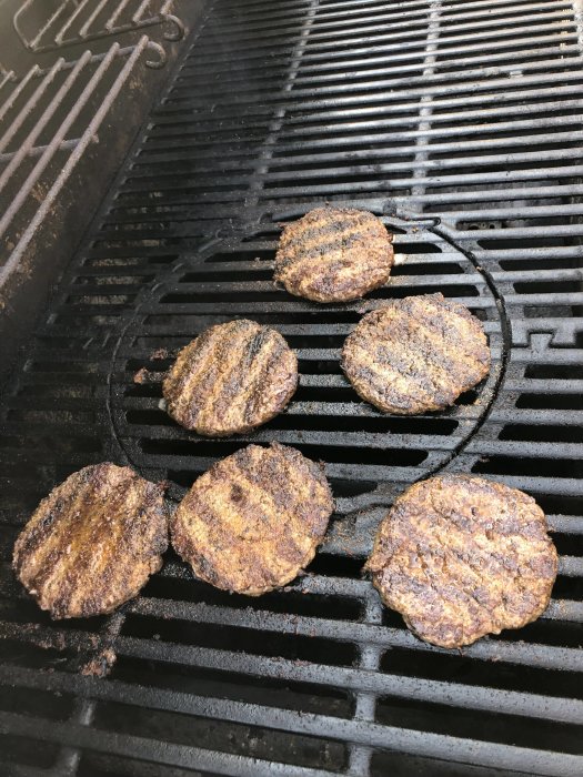 Fem grillade burgare med grillmärken på en grillrist, inget bacon synligt.