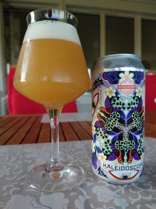 Ölglas med skummad öl bredvid en färgglad Burk av Basqueland Brewing Project's Kaleidoscope DDH IPA.