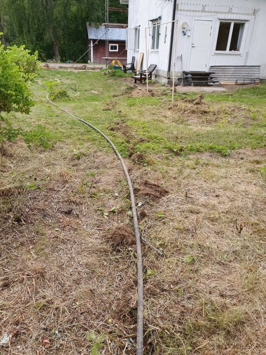 En upptagen vattenslang på en gräsmatta med hus och byggmaterial i bakgrunden.