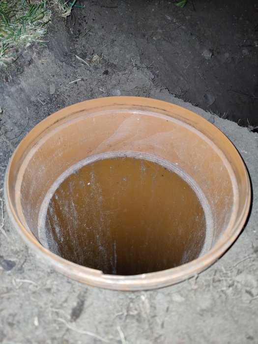 Översiktsbild av ett öppet, brunaktigt plastavloppsrör i marken. Röret är smutsigt med synliga repor inuti.