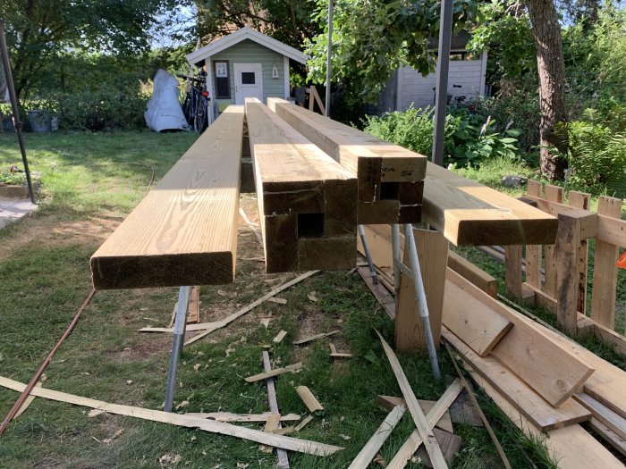 Långa träbrädor upplagda på bockar utomhus med rester från sågning på marken.