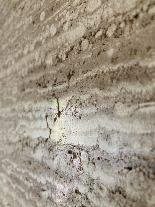 Närbild av en grov och porös stenvägg med möjlig marmorstruktur, skadad med gropar och ojämn yta.