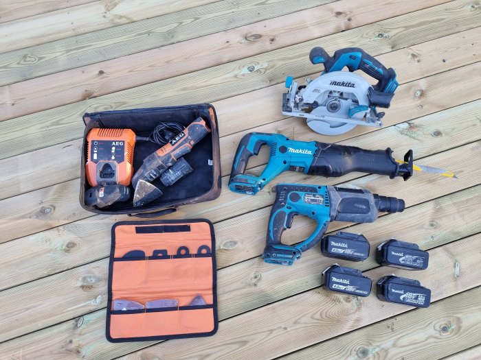 Samling verktyg på trägolv, inklusive borr, såg och batterier.