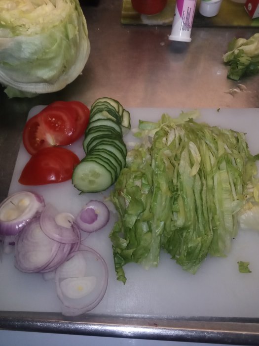 Skivade grönsaker på en skärbräda inklusive rödlök, tomat, gurka och sallad.
