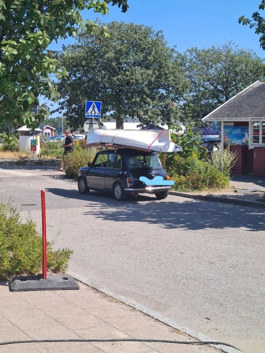 Liten bil parkerad på gata med stor kanot säkrad på taket.