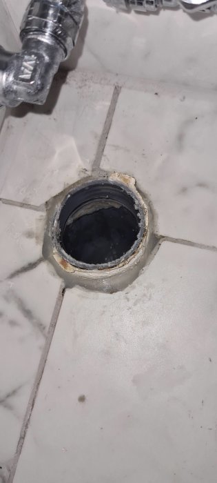 Ett rörstick upp ur ett kaklat golv, snett kapad och sticker upp cirka 1 cm med synlig gummimuff.