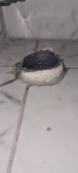 Snett kapad röruppstick ca 1 cm högt i våtrum med synlig gummimuff och ojämnt tätningsskikt.
