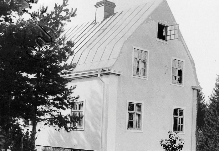 Svartvit bild av hus från 1920-talet med originalfönster och fönsterluckor, putsad fasad.