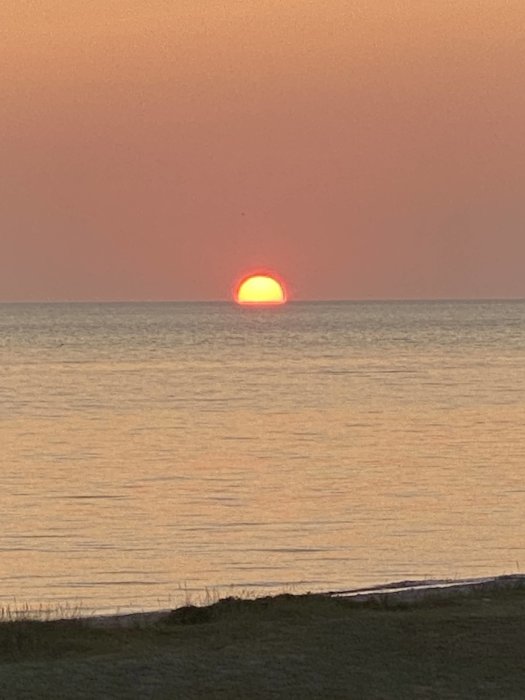 Solnedgång över havet med röd sol halvt nedsänkt i horisonten och färgat himlen orange.