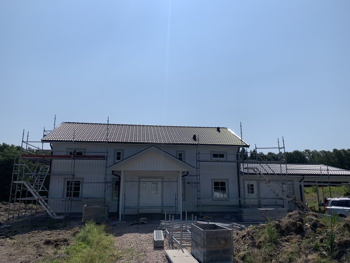 Hus under renovering med pågående målningsarbete och nedmonterad ställning vid carporten.