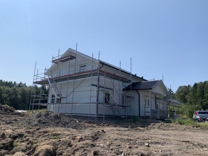 Hus under renovering med byggställningar runt fasaden och omgivet av skog och öppen mark.