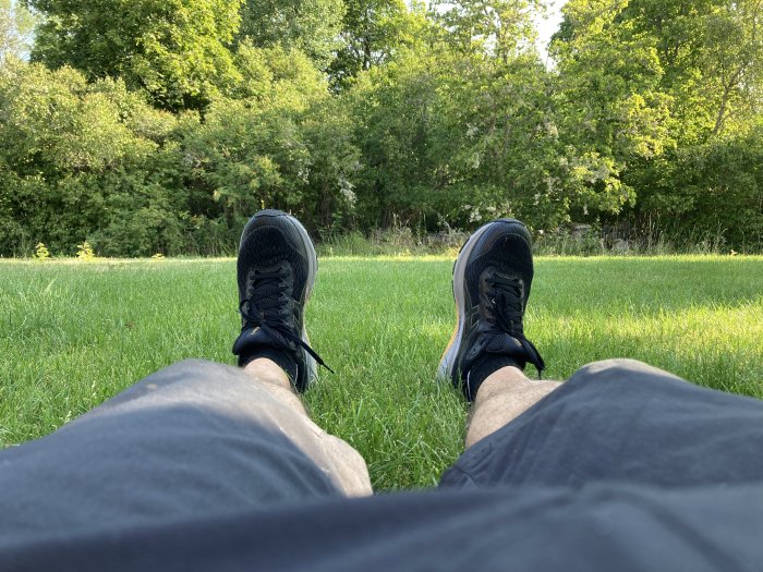 Person som vilar på gräsmatta med benen utsträckta, synliga sneakers och grönska i bakgrunden.