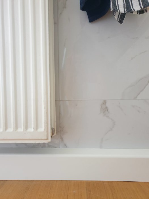 Renoverat rum med vitmarmorerade kakelplattor vid en radiator samt parkettgolv och vit sockel.
