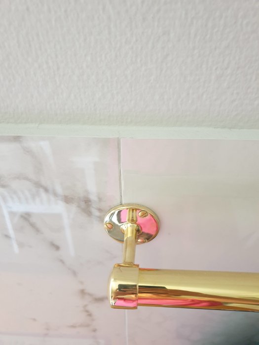 Guldig handdukshållare monterad på marmormönstrad vägg under vitmålad list.