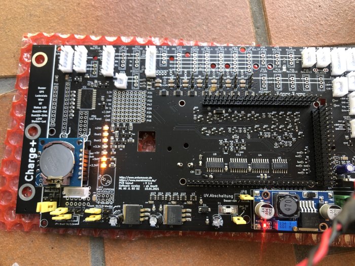 Elektronikmodul med lysdioder och kablar på en röd bobbleplastbakgrund under test.