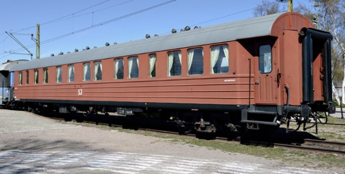 Gammal rödbrun personvagn från SJ med välstoppade säten och öppningsbara dörrar.