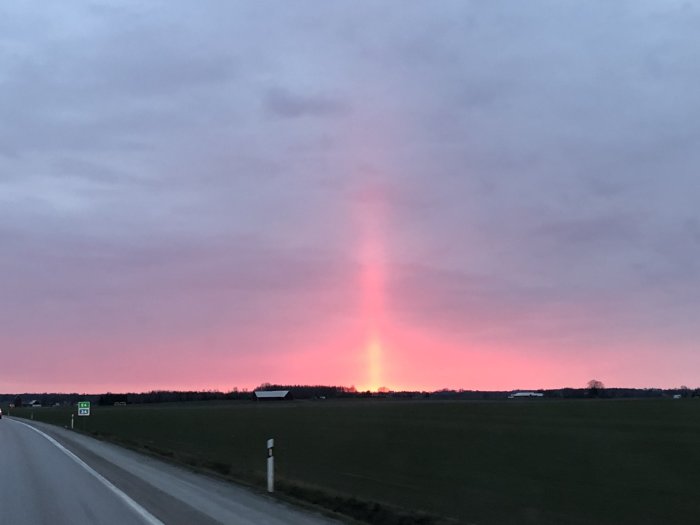 Solnedgång med vertikalt ljusfenomen över ett landskap vid E4 nära Linköping, spegling möjlig från sjön Boren.