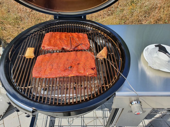 Spare ribs med rub i Texas-stil på grillen, med rökträ och termometer.