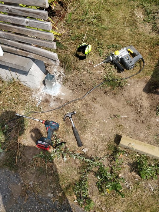 Verktyg på marken vid installation av grindfästen, inklusive borr, måttband och hammare.