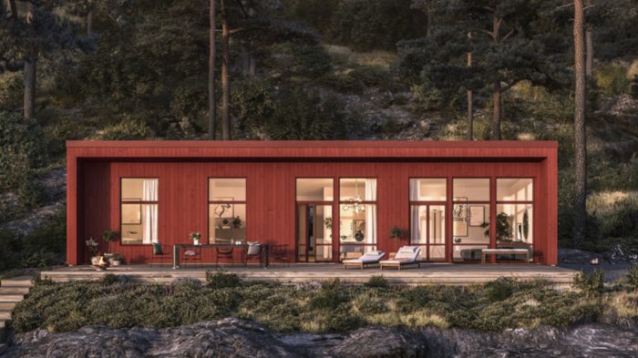 En röd modern villa med stora fönster intill en skog på kvällen.